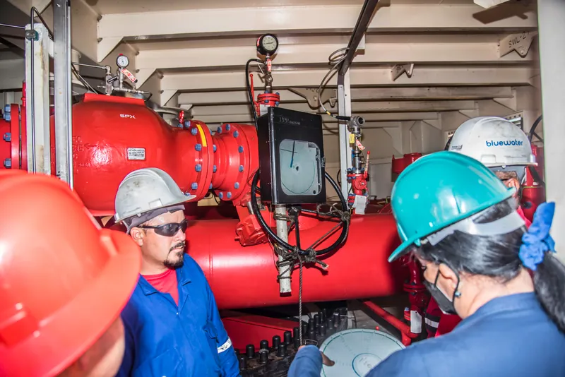 Equipo técnico inspeccionando instrumentación y válvulas en la sala de bombas de un terminal marítimo.